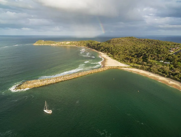 Ocean coastline with boat and rainbow at sunset