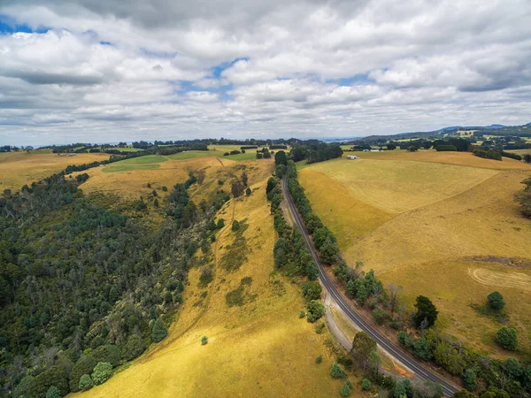 オーストラリアの田舎で黄色の圧延丘の間の農村道路の空中風景 — ストック写真