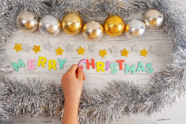 Childs hand makes Christmas composition colorful text Merry Christmas ornated with baubles and tinsel - top view
