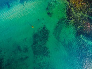 Sığ turkuaz şeffaf okyanus suyuna ve küçük sarı balıkçı teknesine bakıyorum.