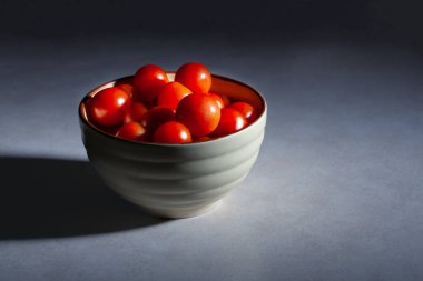 Çeri domatesler seramik kasede spot ışıkları altında fotokopi alanı olan bir masada.