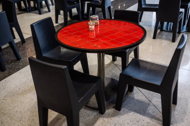 Alışveriş merkezinde siyah sandalyeli kırmızı yuvarlak masa.