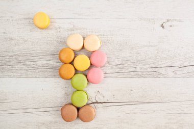 Çiçek ve güneş beyaz kırsal ahşap masa üzerindeki renkli badem kurabiyelerinden yapılmıştır.