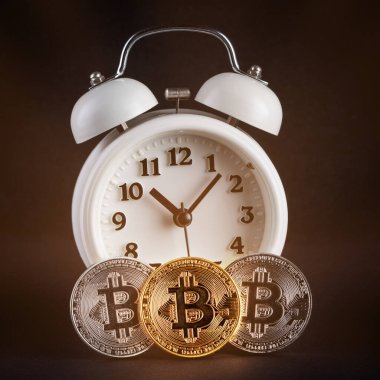 Siyah arka planda parlayan üç bitcoin ve antika beyaz alarm saati