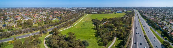 Aerial panoramic landscape of cars driving on highway passing through typical suburban landscape in Melbourne, Australia