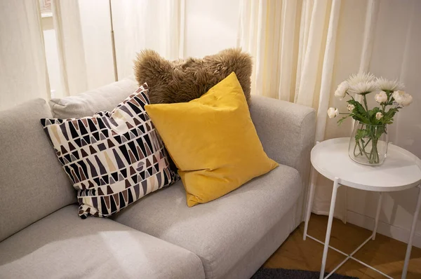浅灰纺织品沙发上的装饰枕头 白色侧桌和花朵 舒适的室内设计 — 图库照片