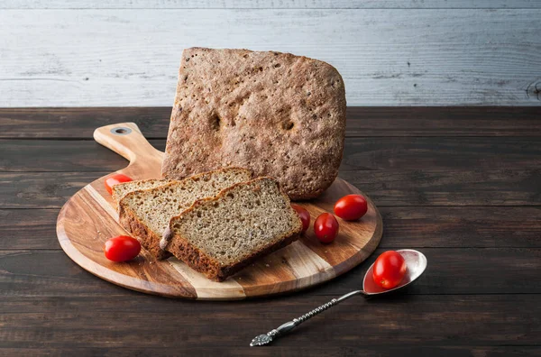 Dark rye homemade bread with cherry tomatoes on round chopping board and copy space