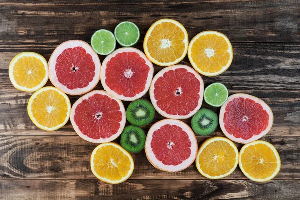 Slices of red grapefruit, lime, orange, and kiwi arranged on rustic wooden table. Top view.