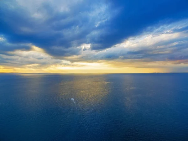 Aerial view of lonely boat sailing across ocean at beautiful sunset