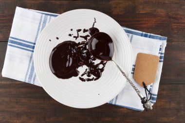 Beyaz tabakta erimiş çikolatayla kaplanmış klasik kaşık ve hediye etiketli ahşap masa. Üst görünüm.