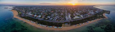 Brighton banliyösündeki gündoğumunun hava manzarası ikonik sahil kulübelerini, evleri ve okyanusu gösteriyor. Melbourne, Victoria, Avustralya