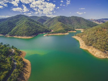 Güneşli bir günde, ormanlık tepelerin arasında güzel bir göl.