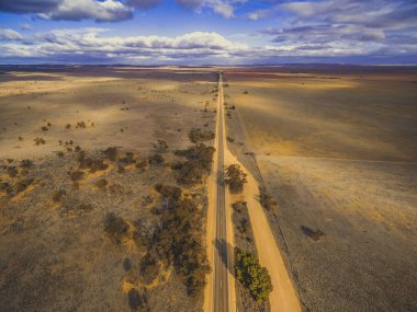 Güney Avustralya ovalarından düz kırsal yol geçiyor. Bulutlar karada güzel gölgeler bırakıyor. Hava manzarası.