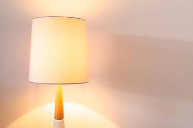 Beyaz abajurlu yatak odası lambası kopyalama alanı olan beyaz duvara karşı yanıyor.