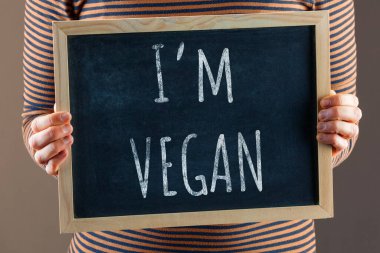 Kadın elleri vücudun önünde küçük siyah bir karatahta tutuyor ve vegan olduğumu söylüyor.