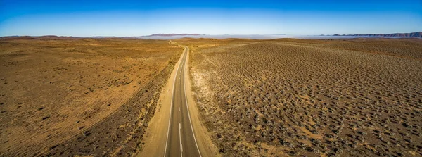 日の出に植生の少ない乾燥した土地を通過する農村道路 広い空中パノラマ — ストック写真
