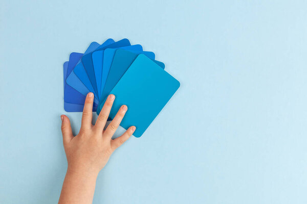 Child's hand touching color samples cards - hues of blue. Top view with copy space