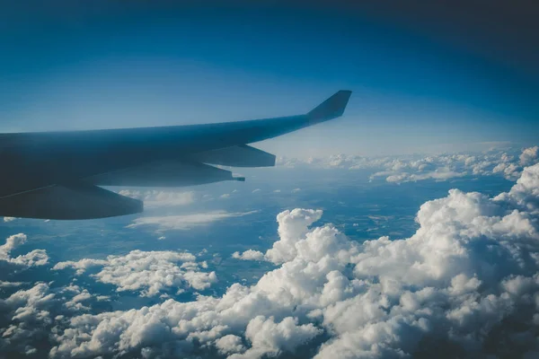 ふわふわした雲と遠くの地球上の飛行中の大型旅客機の翼 — ストック写真