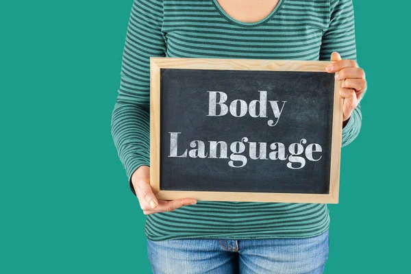 Female hands holding small black chalkboard in front of the body with written words saying Body Language
