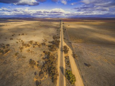 Güney Avustralya ovalarından düz kırsal yol geçiyor. Bulutlar karada güzel gölgeler bırakıyor. Hava manzarası.