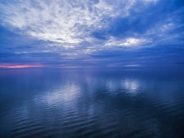 Blue dusk over ocean with clouds reflecting in the calm waters clipart