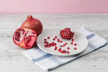 Nar bir bütün, yarısı ve tohumlar beyaz tabağa saçılmış, kırsal ahşap masa.