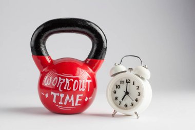 Red kettlebell with Workout Time lettering written on it and traditional alarm clock isolated on white with copy space. Time to work out, healthy lifestyle concept clipart