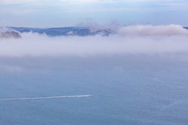 Küçük tekne okyanusu aşıp alçak bulutların altında su izi bırakıyor.