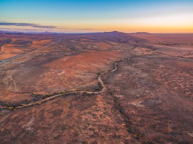 Mars 'a benzeyen, kıvrımlı çakıl yolu olan kırmızı gökyüzü üzerinde gün batımını gösteren hava manzarası.