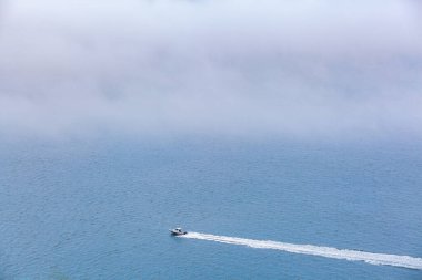 Küçük tekne okyanusu aşıyor. Alçak bulutların altında kopya alanı olan su izi bırakıyor.