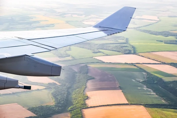 明るい太陽ともやの中で農地のパッチワークの上を飛ぶ旅客機の大きな翼 — ストック写真