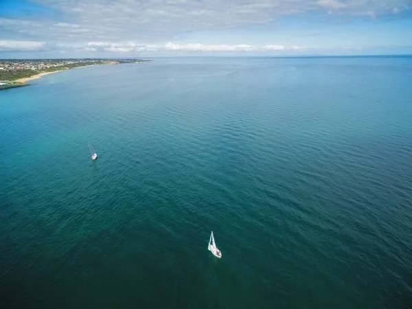 Aerial image of two sailboats sailing turquoise waters