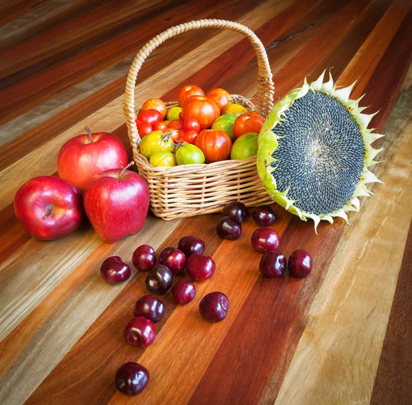 Small tomatoes, cherries, apples, and ripe sunflower. Healthy organic food composition on a wooden table