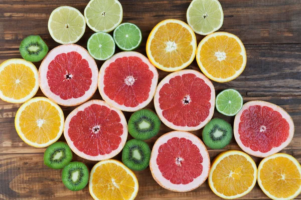 Slices of red grapefruit, lime, orange, lemon, and kiwi arranged on rustic wooden table closeup. Top view.
