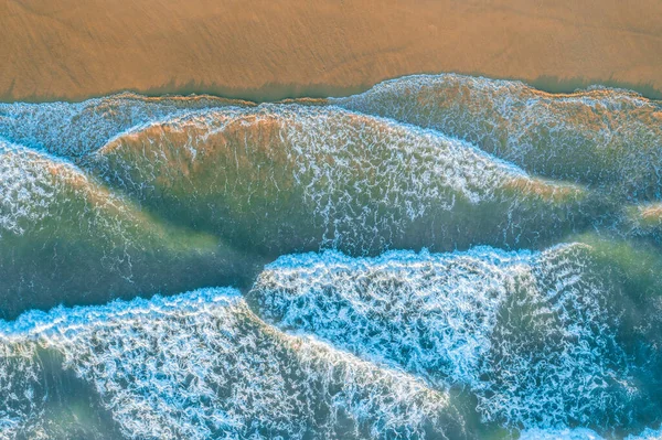 Looking down at ocean waves roll and crash into the shore at sunrise