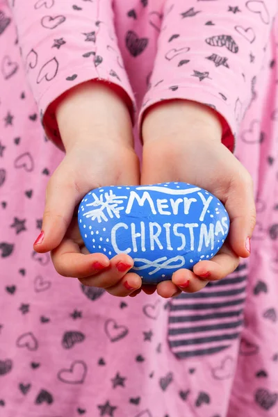 Merry Christmas hand lettering greeting on painted stone in hands of young girl closeup