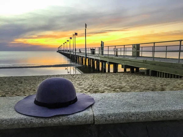 Ladys hat on concrete ledge and long pier at sunset