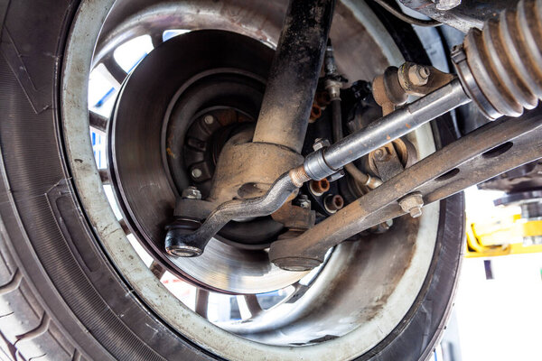 Крупный план внутренней части колеса автомобиля с амортизатором, регулирующим рычагом, CV валом и другими механическими деталями во время планового осмотра в цехе
