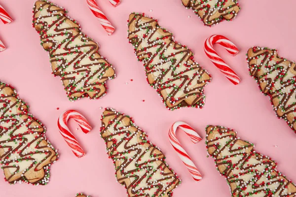 Christmas sweet food theme - christmas trees biscuits with candy canes on pink background, top view