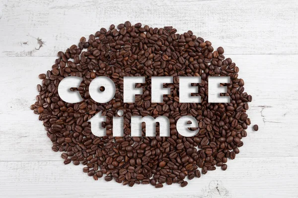 Coffee time text on scattered roasted coffee beans on white rustic wooden background