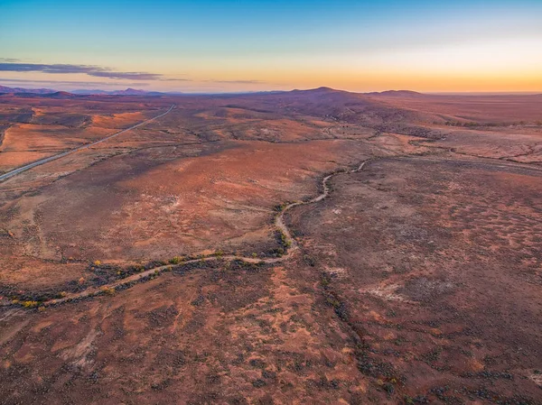 Mars 'a benzeyen, kıvrımlı çakıl yolu olan kırmızı gökyüzü üzerinde gün batımını gösteren hava manzarası.