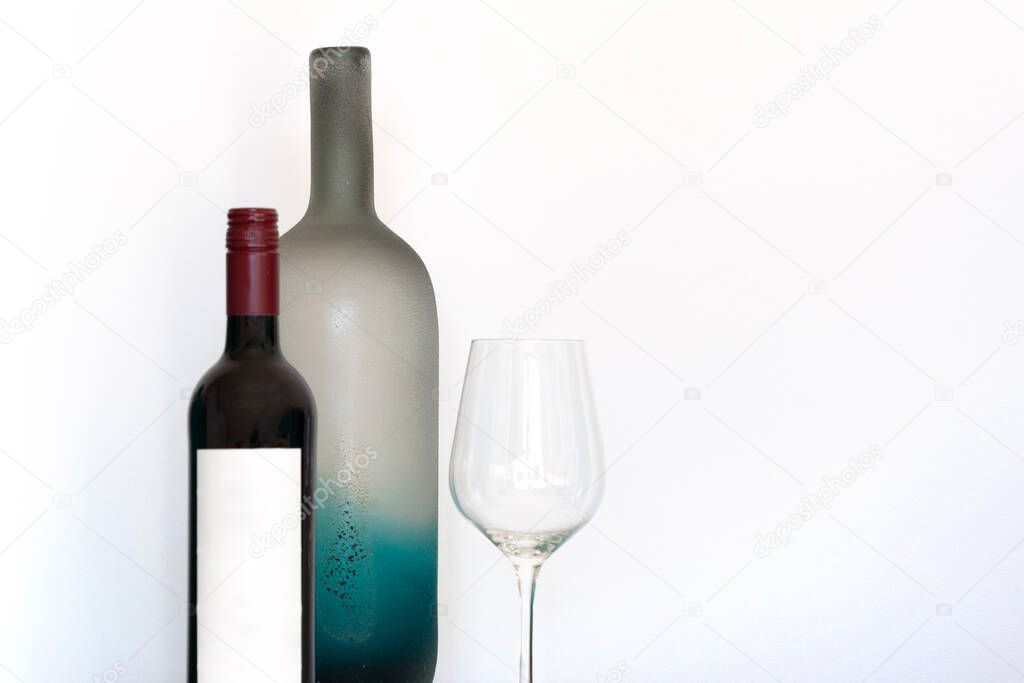 Wine bottle with empty label, wineglass and decorative frosted glass bottle on white background with copy space