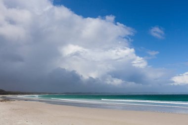 Fırtınalı bulutların ve mavi gökyüzünün altında beyaz kumlar güzel okyanus plajı