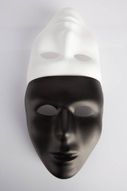 Siyah ve beyaz maskeler beyaz yansıtıcı arka planda birleşti. Dikey görüntü, üst görünüm. Anonimlik kavramı.