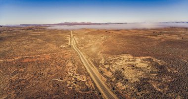 Countryside highway passing through Australian outback desert leading to mountains - aerial panorama clipart