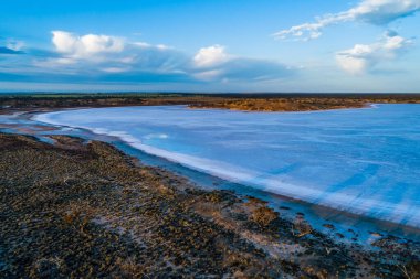 Avustralya kırsalında güneş doğarken sığ tuz gölünün üzerindeki uzun ağaç gölgeleri