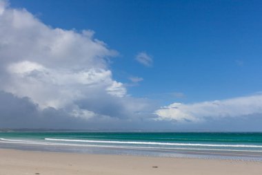 Fırtınalı bulutların ve mavi gökyüzünün altında güzel okyanus sahilindeki beyaz kum.