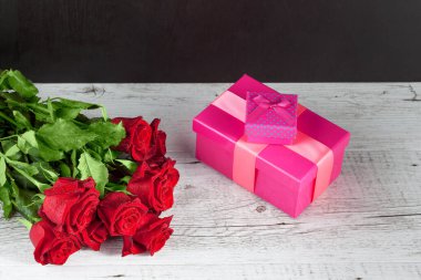 Kırmızı güller buketi ve pembe hediye kutuları beyaz kırsal ahşap masa üzerinde fotokopi alanı ile