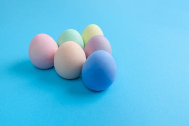 Paskalya yumurtaları, mavi arkaplan üzerinde üçgen şeklinde düzenlenmiş sade renklere boyanmış.