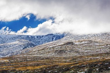 Kabarık bulutların altında karla kaplı dağlar